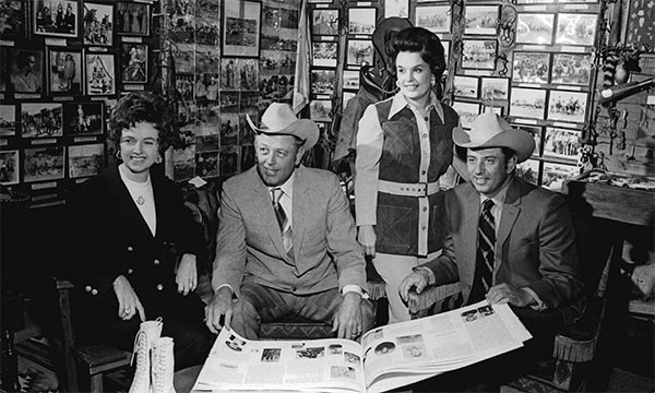 Black and white photograph inside the Saunders Ranch Museum. Left to right: Jane Saunders Calhoun, James M. Calhoun, Ann Osborne Saunders, and Tom B. Saunders IV.