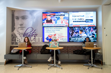 Three students with laptops sitting in front of the Bistro Burnett sign.