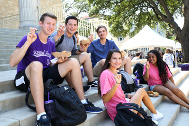 Students sitting on steps, posign with the TCU Frog symbol.